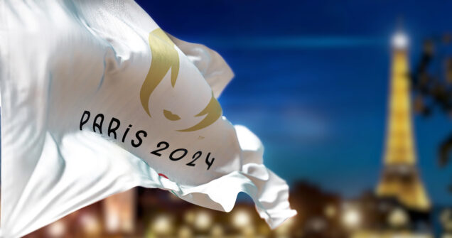 Paris, FR, Jan 2023: Paris 2024 Summer Olympics flag waving in the wind with blurred Paris skyline on the background at night. Realistic 3d illustration. Illustrative editorial